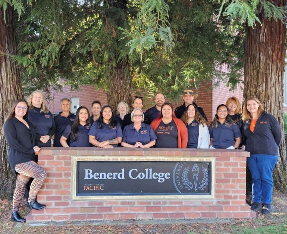The staff of Benerd College standing behind the Benerd sign